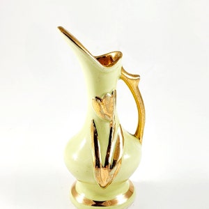 May include: A small, pale green ceramic pitcher with gold accents. The pitcher features a curved spout, a handle, and gold floral designs. The base and rim are also trimmed with gold. A decorative piece.