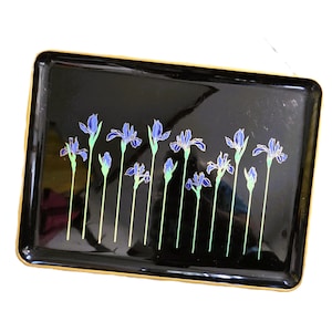 May include: A rectangular black tray with a glossy finish, featuring a series of purple iris flowers with green stems and leaves printed across the center. The tray has a thin gold-colored border along the outer edge of its raised rim.