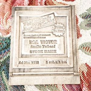 May include: A gray, rectangular advertisement for RCA Victor radio tubes. The ad features the text "For New Pep in Your Old Radio!" and "Phone Us Now!" along with the RCA Victor logo and the words "Radio Tubes!" and "Store Name."