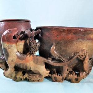 May include: A carved stone sculpture featuring a tiger, grapes, and a bird. The sculpture has a reddish-brown and tan color palette. The tiger is in the foreground, with a detailed carving of a bird and grapes on the side.