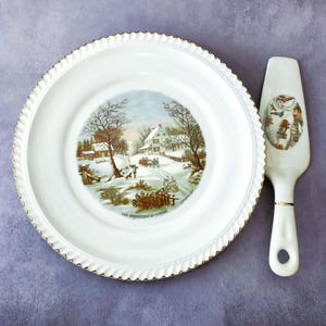 May include: White ceramic plate and cake server set. The plate features a winter scene with a house, trees, and text that reads "The Homestead in Winter." The plate has a gold rim. The cake server has a matching winter scene.