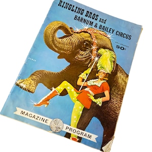 May include: A vintage Ringling Bros and Barnum & Bailey Circus magazine program from the 84th season. The cover features a large grey elephant and a performer in a red tunic and green leggings holding a feathered wand against a light blue background.