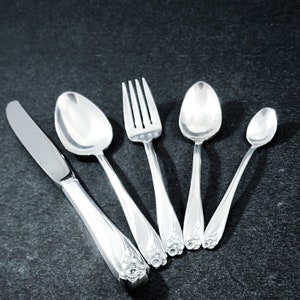 May include: A set of five silver-plated utensils, including a knife, fork, and three spoons. The utensils have ornate floral designs on the handles.
