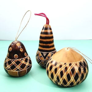 May include: Three handcrafted gourd ornaments with intricate etched designs. One is pear-shaped with a dot pattern, another is striped, and the third is round with a diamond pattern. Each has a string for hanging.