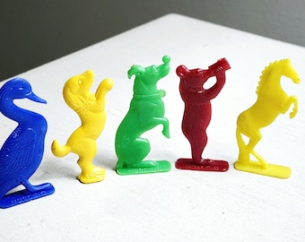 May include: A row of five colorful plastic animal figurines: a blue duck, a yellow dog, a green dog, a red bear, and a yellow horse. Each figurine is standing on a small base. The figurines are in a row on a white surface.