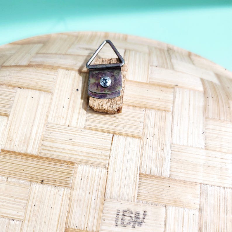 May include: Close-up of the back of a woven bamboo object, featuring a metal hanger attached with a screw. The bamboo has a natural, light brown color and a textured, basket-weave pattern. The hanger is silver.