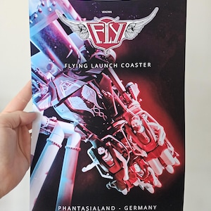 May include: A rectangular poster featuring the F.L.Y. flying launch coaster at Phantasialand, Germany. The graphic displays a red and blue color scheme with a winged logo at the top, the text "VEKOMA", "FLY", "FLYING LAUNCH COASTER", and "PHANTASIALAND - GERMANY".