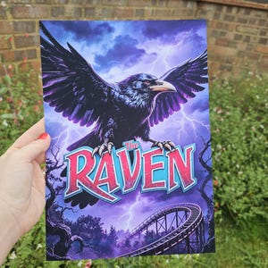 May include: A rectangular art print featuring a large black raven with spread wings flying against a dark purple stormy sky with lightning bolts. Below the bird, the text "The RAVEN" is displayed in bold red and blue letters above a roller coaster.