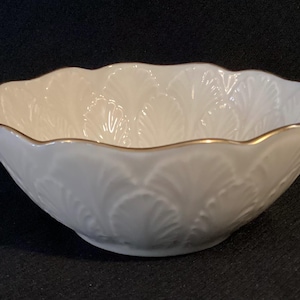 May include: A white, scalloped-edge bowl with a gold rim. The bowl features a delicate, embossed leaf pattern on its exterior. The bowl is likely made of porcelain or a similar ceramic material, and is suitable for serving or display.