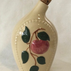 May include: A cream-colored ceramic bottle with a cork stopper. The bottle has a raised design of a red apple with green leaves on a vine.