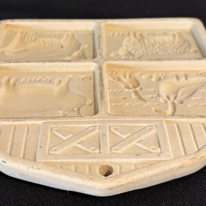 Puede incluir: Salvamanteles rectangular de cer&aacute;mica color crema con cuatro secciones empotradas, cada una representando una escena de granja. La secci&oacute;n inferior presenta un dise&ntilde;o tipo granero con una abertura para colgar. El salvamanteles es probablemente vintage.