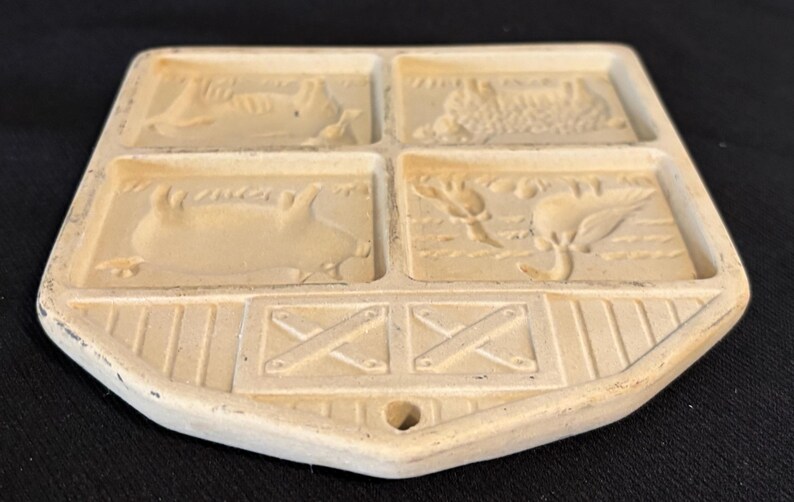 Puede incluir: Salvamanteles rectangular de cer&aacute;mica color crema con cuatro secciones empotradas, cada una representando una escena de granja. La secci&oacute;n inferior presenta un dise&ntilde;o tipo granero con una abertura para colgar. El salvamanteles es probablemente vintage.