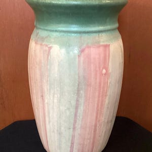 May include: A ceramic vase with a green rim and pink and white vertical stripes. The vase is a light green color with a glaze that gives it a textured look.
