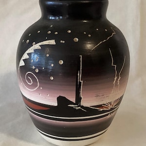 May include: A black ceramic vase with a night sky design. The vase features white stars, a spiral, and a landscape with a mountain and lightning bolts. The base has a white stripe. The vase is approximately 8 inches tall.