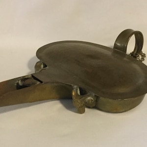 May include: A brass oil lamp with a hinged lid and a spout. The lamp has a handle with a chain attached to it.