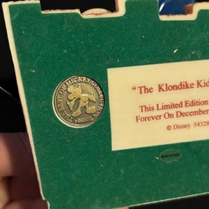 May include: A green and off-white collectible featuring a gold-colored Mickey Mouse emblem that reads "The Best of Mickey Collection." The text "The Klondike Kid" is visible, along with "This Limited Edition" and "Forever On December."