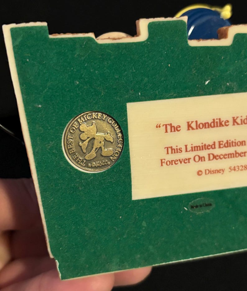 May include: A green and off-white collectible featuring a gold-colored Mickey Mouse emblem that reads "The Best of Mickey Collection." The text "The Klondike Kid" is visible, along with "This Limited Edition" and "Forever On December."