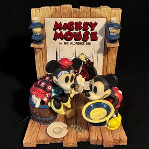 May include: A vintage Mickey Mouse figurine from "The Klondike Kid" featuring Mickey and a friend. The figurine has a wooden frame with two small blue lamps. The year "1932" is printed on the base. Mickey is wearing a red hat and a patterned outfit.