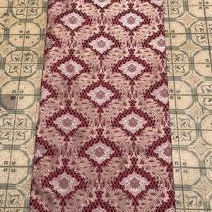 May include: A burgundy table runner with a white and gold floral pattern and white fringe trim.