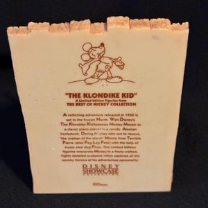 May include: A collectible figurine from the Disney Showcase Collection. The figurine features Mickey Mouse from "The Klondike Kid." The text on the figurine describes the 1932 adventure set in the frozen North. The figurine is a limited edition.