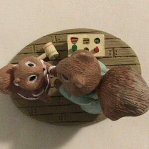 Puede incluir: Una figurita de dos ardillas marrones jugando a un juego con un martillo de madera y un juguete de clasificaci&oacute;n de formas. Las ardillas llevan ropa azul y morada y est&aacute;n sentadas en una plataforma de madera.