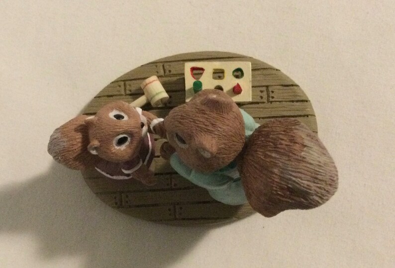 Puede incluir: Una figurita de dos ardillas marrones jugando a un juego con un martillo de madera y un juguete de clasificaci&oacute;n de formas. Las ardillas llevan ropa azul y morada y est&aacute;n sentadas en una plataforma de madera.