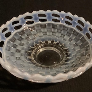 May include: An opalescent glass basket with a woven pattern and a scalloped rim. The rim has a series of oval cutouts. The basket's interior is clear, and the rim has a blueish hue. The basket is likely vintage.