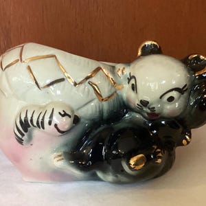May include: A vintage ceramic planter in the shape of a panda bear and cub. The panda is black and white with gold accents. The planter has a cracked eggshell design with gold trim and a pink base.