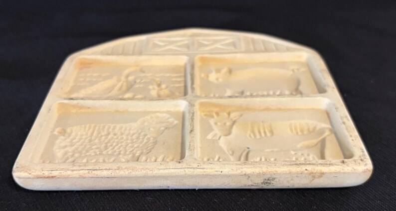 Puede incluir: Molde de mantequilla rectangular de color crema, con cuatro dise&ntilde;os de animales: un pato, un cerdo, una oveja y una vaca. El molde tiene una parte superior en forma de granero con detalles de entramado. Dise&ntilde;o r&uacute;stico y vintage.