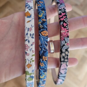Peut inclure: Trois bandeaux en tissu &agrave; motifs floraux. Le bandeau de gauche a un fond blanc avec des fleurs roses, orange et vertes. Le bandeau du milieu a un fond bleu fonc&eacute; avec des fleurs orange, jaunes et bleues. Le bandeau de droite a un fond noir avec des fleurs roses, blanches et vertes.