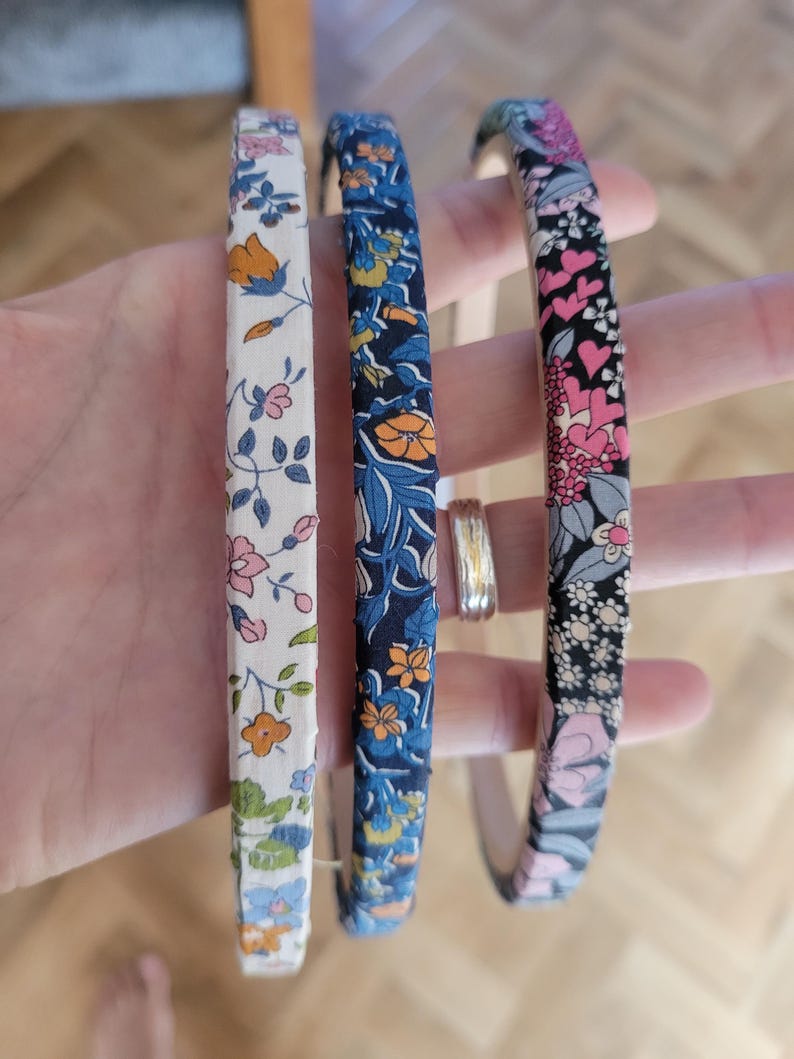 Peut inclure: Trois bandeaux en tissu &agrave; motifs floraux. Le bandeau de gauche a un fond blanc avec des fleurs roses, orange et vertes. Le bandeau du milieu a un fond bleu fonc&eacute; avec des fleurs orange, jaunes et bleues. Le bandeau de droite a un fond noir avec des fleurs roses, blanches et vertes.