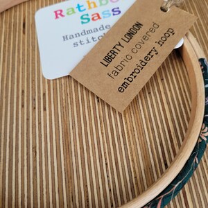 Peut inclure: Un cerceau de broderie en bois avec un rev&ecirc;tement en tissu pr&eacute;sentant un motif floral dans des tons de vert et de rose. Le cerceau est &eacute;tiquet&eacute; "Liberty London tissu recouvert de broderie" et "Rathbone Sass Couture faite main".