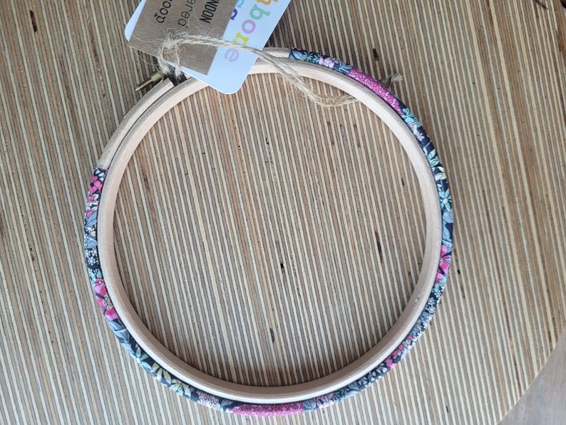 Peut inclure: Un cercle &agrave; broder en bois recouvert d'un tissu floral. Le tissu est un m&eacute;lange de rose, de noir et de blanc.