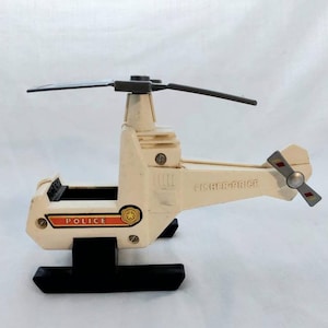 May include: White plastic toy helicopter with black landing skids and a red and white "POLICE" label. The helicopter has a gray rotor blade and a red and white tail rotor. The toy is labeled "Fisher-Price".