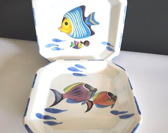 Puede incluir: Dos platos octogonales de cerámica con fondo blanco, borde azul e ilustraciones de peces coloridos. Uno presenta un pez azul y amarillo, el otro peces morados y naranjas. Acentos de olas azules rodean los peces.