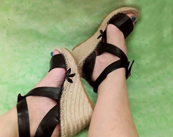 Sandały espadryle z szerokimi skórzanymi paskami. Sandały z krzyżującymi się paskami wokół kostki. Espadryle na wysokim koturnie. Koturny wykonane z trawy esparto i skóry ekologicznej garbowanej roślinnie.