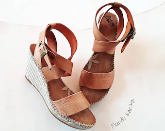 Sandale mit breiten, gekreuzten Riemen. Espadrille-Sandale mit Knöchelriemen. Sandalen aus pflanzlich gegerbtem Leder. Jute-Espadrille mit hohem Keilabsatz. Öko-Sandale