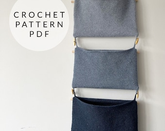 May include: Three crocheted wall pockets hanging on a white wall. The top two pockets are gray and the bottom pocket is black.