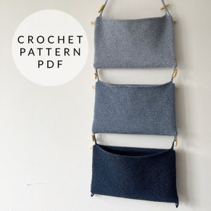 May include: Three crocheted wall pockets hanging on a white wall. The top two pockets are gray and the bottom pocket is black.