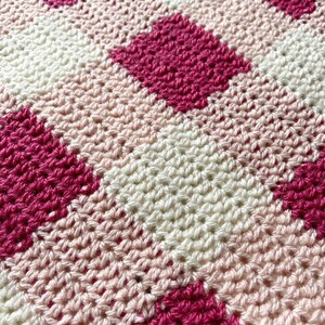 Pode incluir: Um cobertor de croch&ecirc; com um padr&atilde;o xadrez em rosa, branco e rosa claro.