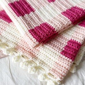 Pode incluir: Um cobertor de beb&eacute; em crochet rosa e branco com uma borda em crochet branco. O cobertor tem um padr&atilde;o xadrez.