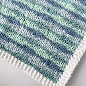 K&ouml;nnte beinhalten: Eine geh&auml;kelte Babydecke mit einem wei&szlig;en Rand und Streifen aus blauem und gr&uuml;nem Garn.