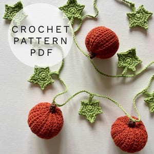 Può includere: Modello all'uncinetto PDF con una ghirlanda con zucche arancioni e foglie verdi a forma di stella. Le zucche sono rotonde e strutturate, collegate da un viticcio verde. Il testo "CROCHET PATTERN PDF" è in un cerchio bianco.