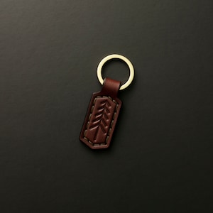 May include: A brown leather keychain with a gold metal ring and a tree design.