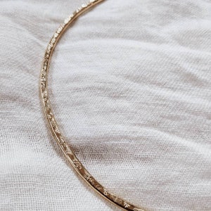 May include: A gold-toned, textured metal choker necklace. The necklace is a simple, minimalist design.