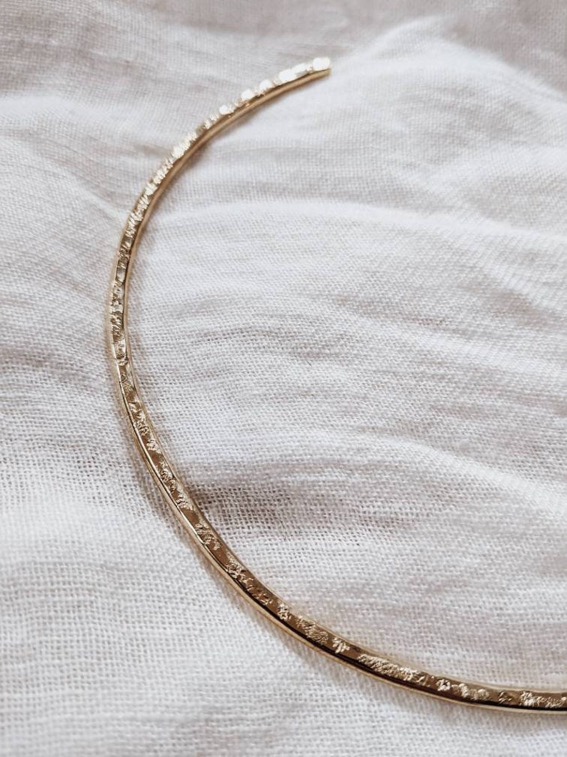 May include: A gold-toned, textured metal choker necklace. The necklace is a simple, minimalist design.