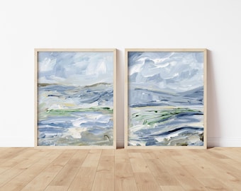 May include: Two framed abstract landscape paintings in shades of blue, green, and white. The paintings are in simple wooden frames and are hung on a white wall.
