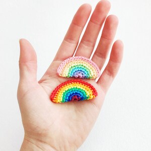 May include: Two crocheted rainbow-coloured arches, one pink and one red, on a white background.