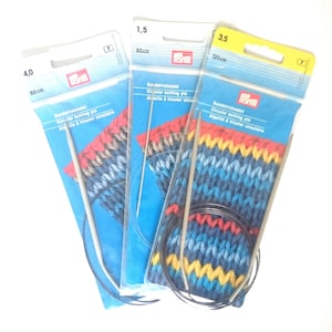 Può includere: Tre confezioni di ferri da maglia circolari nelle misure 4,0 (60 cm), 1,5 (80 cm) e 3,5 (120 cm). Le confezioni sono blu e gialle con il nome del marchio "Frym" stampato su di esse. Ogni confezione include un paio di ferri e un campione di tessuto a maglia.