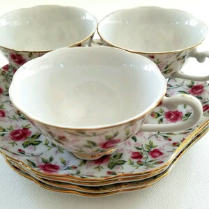 May include: Three white teacups with floral patterns and gold trim, stacked on top of each other. The cups are on a floral patterned saucer.